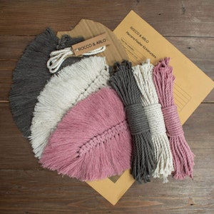 May include: Three macrame feather kits in pink, white and grey. Each kit includes the cord needed to make a feather wall hanging. The kits are packaged in a brown envelope with instructions labelled "Rocco & Arlo Macrame Feather Kit Instructions".