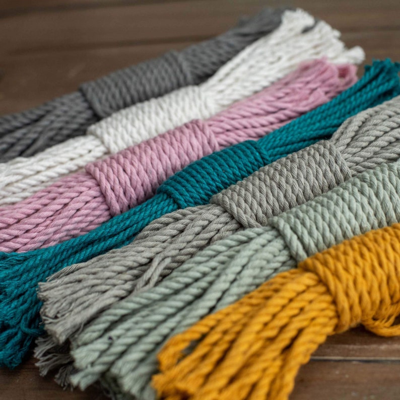May include: A collection of colorful cotton ropes in various shades of gray, pink, teal, green, and yellow. The ropes are arranged in a fan shape, with the ends of the ropes overlapping.