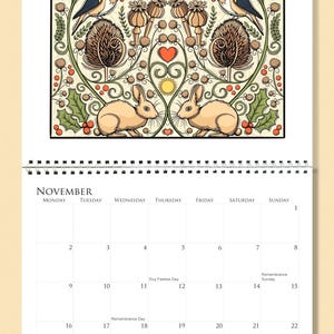 Op de afbeelding: Een kalenderpagina voor november met een decoratieve illustratie van vogels, konijnen en bloemmotieven. De kalender heeft een spiraalbinding en een cr&egrave;mekleurige achtergrond. De illustratie is symmetrisch.