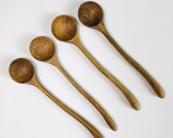 Könnte beinhalten: Vier Holzlöffel mit abgerundeten Schalen und langen, schlanken Griffen sind diagonal auf einer weißen Oberfläche angeordnet. Die Löffel haben eine natürliche Holzmaserung und eine warme, braune Farbe. Die Löffel sind wahrscheinlich für den Küchengebrauch.