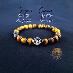 Könnte beinhalten: Ein braunes und goldenes Tigerauge-Armband mit einem silbernen Skorpion-Anhänger. Das Armband ist aus Edelstahl und trägt den Text "Skorpion - Skorpion" und "Tigerauge".