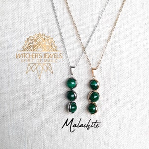Peut inclure: Deux colliers avec des pendentifs en pierre de malachite verte. Les colliers sont sur un fond de tissu blanc. Les colliers sont en argent et en or. Le texte "WITCHER'S JEWELS SPIRIT OF MAGIC" est visible sur l'image. Le texte "Malachite" est visible sur l'image.
