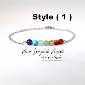 Peut inclure: Un bracelet en chaîne argentée avec sept perles de pierres précieuses colorées. Les perles sont violettes, bleues, vertes, orange, brunes et rouges. Le texte "Style (1)" est au-dessus du bracelet. Le texte "Acier Inoxydable Argente chaine simple" est en dessous du bracelet.