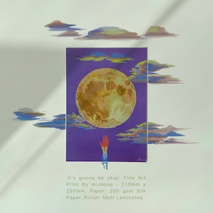 May include: A fine art print of a yellow moon with a hand reaching up towards it. The moon is surrounded by clouds and the background is purple. The print is titled 'It's gonna be okay' and is 210mm x 297mm. The paper is 350 gsm Silk Paper with a Matt Laminated finish.