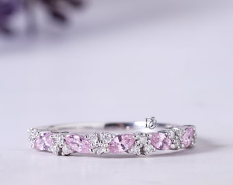 Könnte beinhalten: Ein silberfarbener Ring mit einer Reihe abwechselnder rosafarbener Steine im Marquise-Schliff und kleinen runden, klaren Steinen. Der Ring hat ein zartes, symmetrisches Design mit einem kleinen Logo auf der Innenseite der Ringschiene.