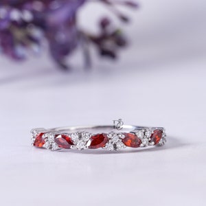 Puede incluir: Un anillo de banda de plata con una fila de piedras preciosas de forma marquesa alternando rojo y blanco.