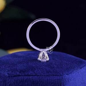 May include: A silver-toned metal ring featuring a thin, circular band and a prong setting that secures a single, clear, faceted gemstone. The ring is positioned vertically, showcasing the profile of the setting and the band's smooth, polished surface.