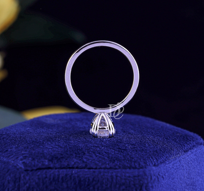 May include: A silver-toned metal ring featuring a thin, circular band and a prong setting that secures a single, clear, faceted gemstone. The ring is positioned vertically, showcasing the profile of the setting and the band's smooth, polished surface.