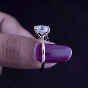 May include: A gold ring featuring a large, round, clear faceted gemstone held in a multi-prong setting. The band is thin and polished, showcasing a side profile view of the stone's elevation and the metal structure connecting it to the ring shank.