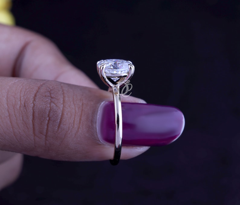May include: A gold ring featuring a large, round, clear faceted gemstone held in a multi-prong setting. The band is thin and polished, showcasing a side profile view of the stone's elevation and the metal structure connecting it to the ring shank.