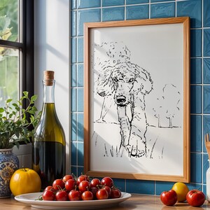 Op de afbeelding: Een zwart-witte lijntekening van een poedel in een lijst hangt aan een blauwe tegelmuur. Een fles olijfolie, een vaas met groen en een bord met rode kerstomaatjes staan op een houten aanrecht.