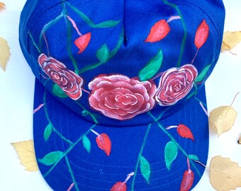 May include: A blue baseball cap with a hand-painted design of pink roses and red leaves.