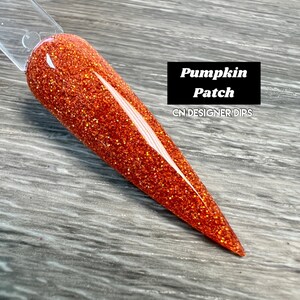 Puede incluir: Primer plano de una uña larga de color naranja con un acabado brillante. La uña está etiquetada como "Pumpkin Patch" y "CN DESIGNER DIPS".