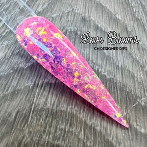 Op de afbeelding: Roze nageldippoeder met gouden en iriserende glitter. Het label luidt "Love Blooms CN Designer Dips."