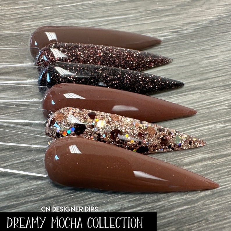 May include: A set of five brown nail dips with different glitter finishes. The dips are arranged in a row, with the glitter finishes increasing in size from left to right. The dips are labeled "Dreamy Mocha Collection" and "CN Designer Dips".