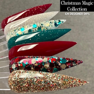 May include: A collection of six long, pointed artificial nails in various colors and glitter designs. The colors include red, white, teal, and gold. The text "Christmas Magic Collection" and "CN DESIGNER DIPS" is displayed in a black box.