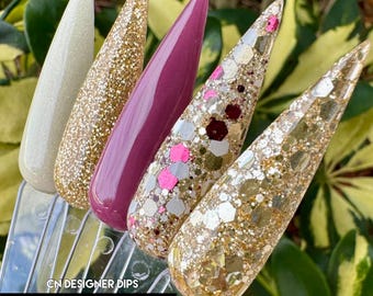 May include: Four nail dip powder colors in a bundle. The colors are a light beige, a gold glitter, a burgundy, and a gold glitter with pink and white accents. The bundle is called "Champagne Kisses Bundle" and is from CN Designer Dips.