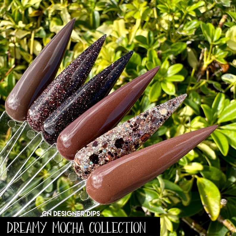 May include: Five different shades of brown nail dip powder, including a glittery brown and a dark brown with glitter. The dips are arranged in a fan shape and labeled "Dreamy Mocha Collection".
