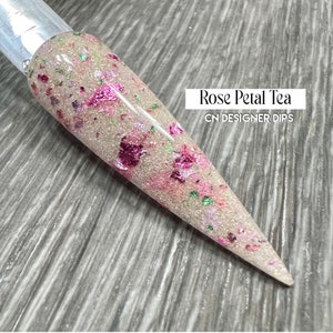 May include: A close-up of a clear nail dip with a light pink base and pink, green, and gold glitter. The text "Rose Petal Tea" and "CN DESIGNER DIPS" is visible in the image.
