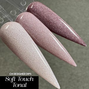 May include: Three nail dip powder colors in shades of pink and white with a gradient effect. The colors are labeled "Soft Touch Tonal" and "CN Designer Dips".