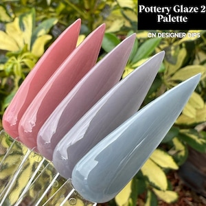 May include: A palette of five long, pointed nail tips showcasing different shades of Pottery Glaze 2. The colors range from a soft pink to a muted blue-gray. The text "Pottery Glaze 2 Palette" and "CN DESIGNER DIPS" is visible.