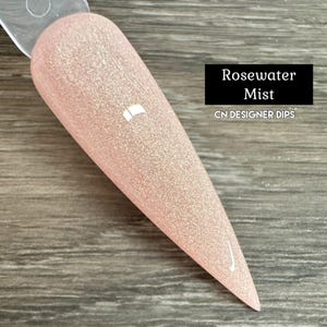 Puede incluir: Primer plano de un esmalte de uñas rosa claro con un acabado brillante. El esmalte se llama "Rosewater Mist" y es un producto de CN Designer Dips.