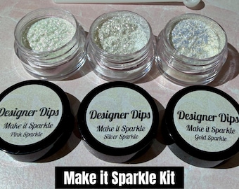 May include: A nail art kit with three jars of glitter, labeled Pink Sparkle, Silver Sparkle, and Gold Sparkle. The jars are clear with black lids and sit below three matching jars filled with glitter. A small scoop is included. The text "Make it Sparkle Kit" is displayed.