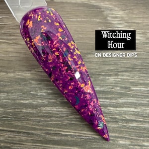 May include: A pointed nail swatch stick featuring a deep purple base color with embedded orange and black foil flakes, plus small crescent moon and star shaped glitter accents. The text Witching Hour and CN DESIGNER DIPS is visible.