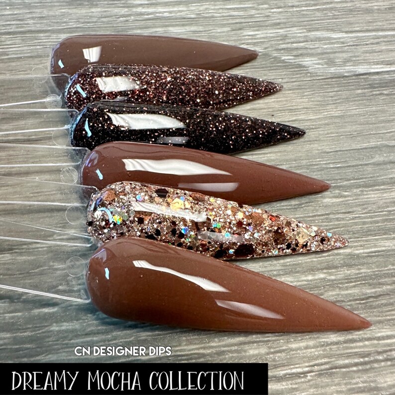 May include: A set of six brown nail dips with glitter accents. The dips are arranged in a row, with the glitter accents on the top of each dip. The dips are labeled "Dreamy Mocha Collection".