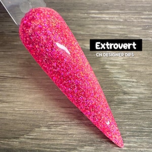 Puede incluir: Un polvo de inmersión para uñas de color rosa con un acabado brillante. La etiqueta dice "Extrovert CN Designer Dips".