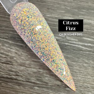 Puede incluir: Primer plano de un polvo de inmersi&oacute;n para u&ntilde;as transparente con purpurina iridiscente. El polvo se llama "Citrus Fizz" y es un CN Designer Dip.