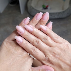 May include: Close-up of hands with light pink nail polish on short, square-shaped nails. The nails are slightly rounded at the edges. The text "The Nail Chambers" is visible on the bottom right of the image.
