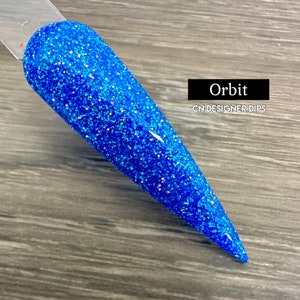 May include: A close-up of a blue glitter nail dip powder with a holographic finish. The powder is labeled "Orbit" and "CN Designer Dips".