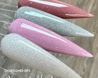 May include: Four nail dip powder colors in a row, from left to right: white with silver glitter, light pink with silver glitter, silver with silver glitter, and a light rose color with silver glitter. The text "CN DESIGNER DIPS Roses Collection" is at the bottom of the image.