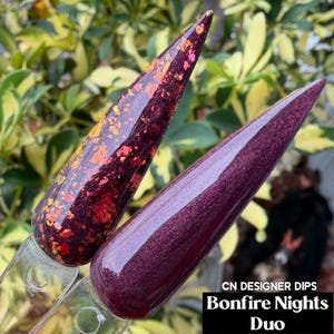May include: Two stiletto-shaped nail swatches displaying the Bonfire Nights Duo. One swatch features a deep burgundy base with iridescent orange and red foil flakes. The second swatch is a solid, shimmering deep plum purple with a smooth finish.
