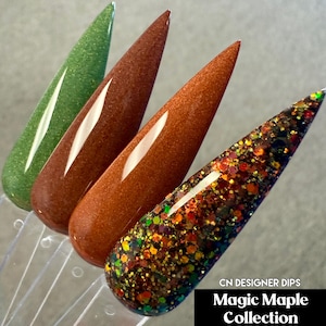 May include: Four nail dip samples in shades of green, brown, and a glittery mix of colors. The samples are arranged in a row, with the text "CN DESIGNER DIPS Magic Maple Collection" in a black box at the bottom.