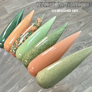 May include: A set of six nail dip powders in shades of green and brown with glitter. The colors are named "Obrecht Rd. Collection" and "CN Designer Dips".