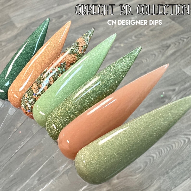 May include: A set of six nail dip powders in shades of green and brown with glitter. The colors are named "Obrecht Rd. Collection" and "CN Designer Dips".