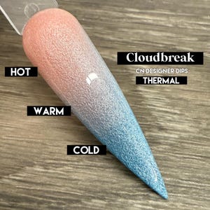 May include: A thermal nail dip powder that changes colour based on temperature. The powder is a light pink colour when warm and a light blue colour when cold. The text "Cloudbreak" and "CN Designer Dips Thermal" is visible on the image.