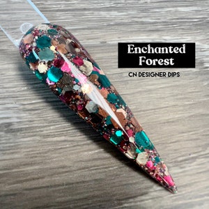Puede incluir: Primer plano de una uña larga y puntiaguda con un revestimiento brillante multicolor. La uña está decorada con una mezcla de purpurina verde, marrón, rosa y dorada. El texto "Enchanted Forest" y "CN Designer Dips" es visible en la imagen.