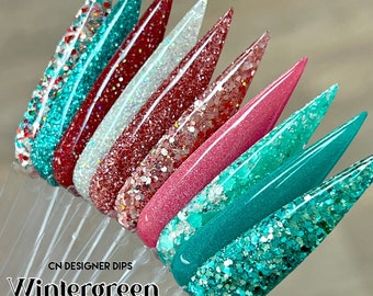 May include: A collection of nail dip samples in various colors, including teal, red, white, and pink, with glitter and shimmer effects. The text "CN DESIGNER DIPS Wintergreen Collection" is displayed at the bottom.