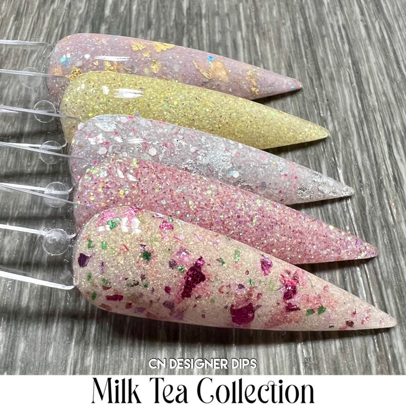 May include: Five nail dip powder colours in a milk tea collection. The colours are a light pink with gold flakes, a light yellow with gold flakes, a light pink with white glitter, a light pink with pink glitter, and a light pink with pink and green glitter.