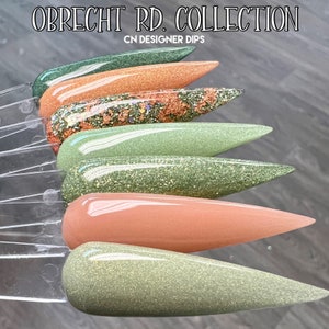 May include: A set of six nail dip powder colors in a variety of green and peach shades. The colors are arranged in a row, with the green shades on the left and the peach shades on the right. The nail dip powders are labeled "OBRECHT RD. COLLECTION CN DESIGNER DIPS".