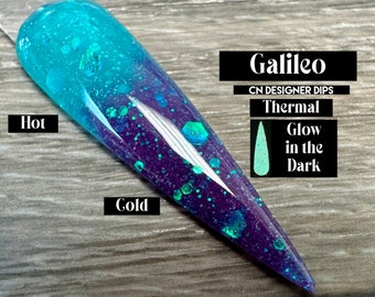 May include: A turquoise and purple nail dip powder with glitter, labeled "Galileo" and "CN Designer Dips". It is a thermal dip powder that changes color with temperature, and glows in the dark. The text "Hot" is written next to the turquoise color, and "Cold" is written next to the purple color.