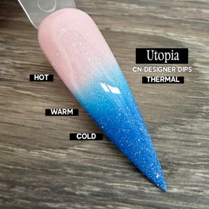 May include: A nail polish swatch stick displaying a thermal color-changing dip powder named Utopia by CN Designer Dips. The pointed tip transitions from a pale pink at the top labeled HOT, through a gradient, to a vibrant blue at the bottom labeled COLD.