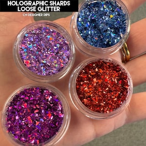 May include: Four small jars of holographic loose glitter. The jars are filled with purple, red, blue, and pink glitter. The jars are labelled "HOLOGRAPHIC SHARDS LOOSE GLITTER CN DESIGNER DIPS".