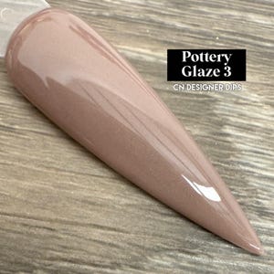 May include: A long, pointed nail dipped in Pottery Glaze 3, a light brown color with a glossy finish. The text "Pottery Glaze 3" and "CN DESIGNER DIPS" are displayed on a black rectangle.