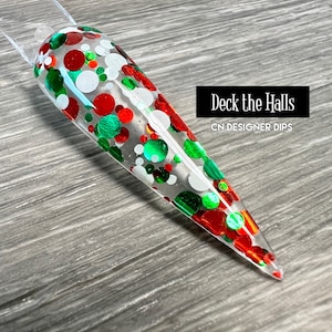 May include: A clear nail dip with red, green, and white glitter in a circular pattern. The text "Deck the Halls" and "CN Designer Dips" is visible in the image.