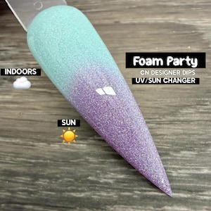 May include: A nail swatch with a glittery gradient design. The top is a light blue, transitioning to purple at the tip. Text on the image reads "Foam Party" and "UV/Sun Changer". The swatch is labeled "Indoors" and "Sun".