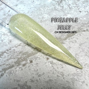 May include: A light yellow nail dip powder with a glittery finish. The powder is called "Pineapple Jelly" and is a CN Designer Dip.